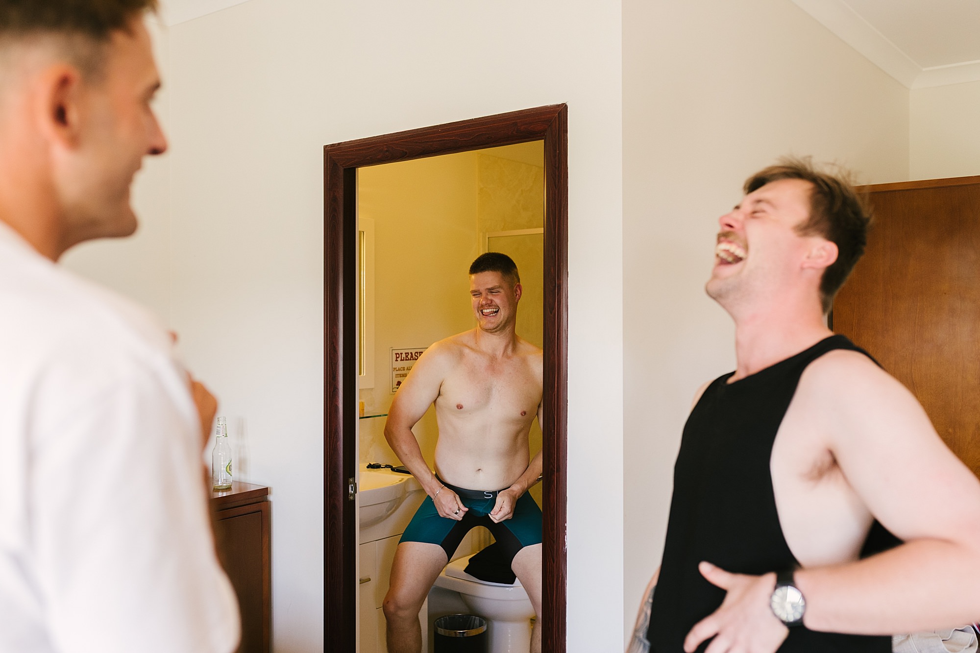 Groomsmen laughing uncontrollably as one makes a cheeky entrance during wedding prep, captured by Bendigo wedding photographer.