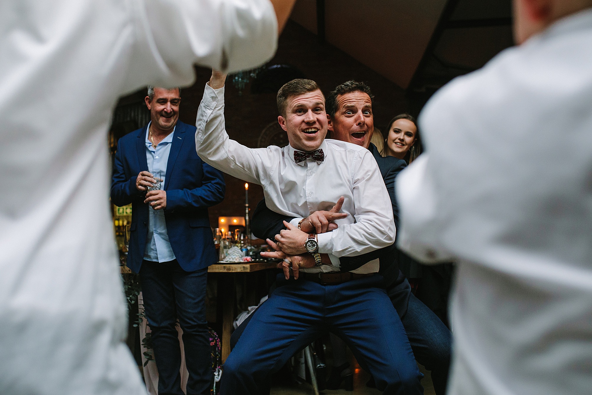 Groom dancing with a guest and playfully challenging two young boys on the dance floor during the wedding celebration.