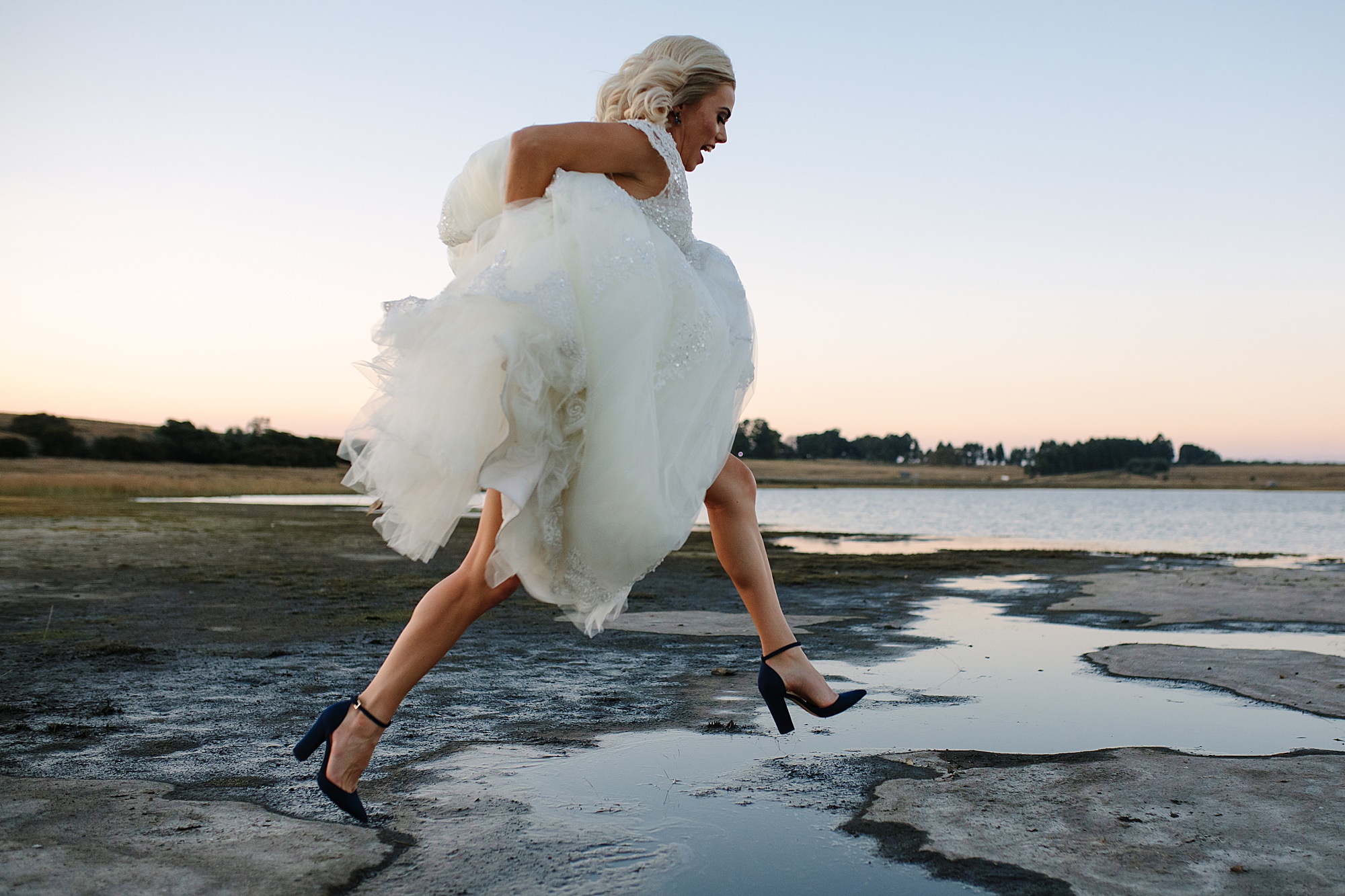 Bride holding her dress and jumping over a water puddle in a salt pan, captured in a spontaneous and exciting moment. 