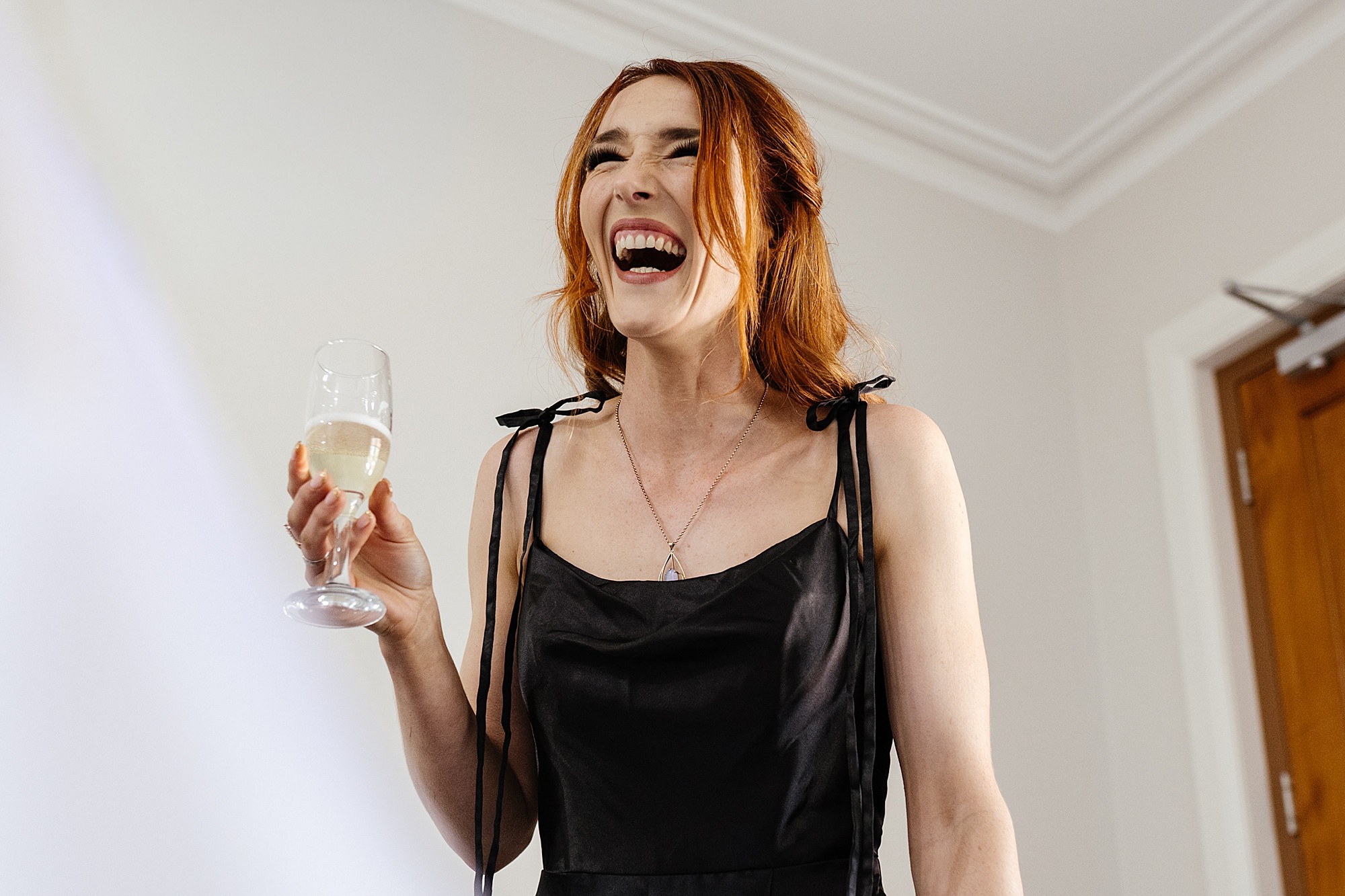Redheaded woman laughing happily while holding a glass of champagne.