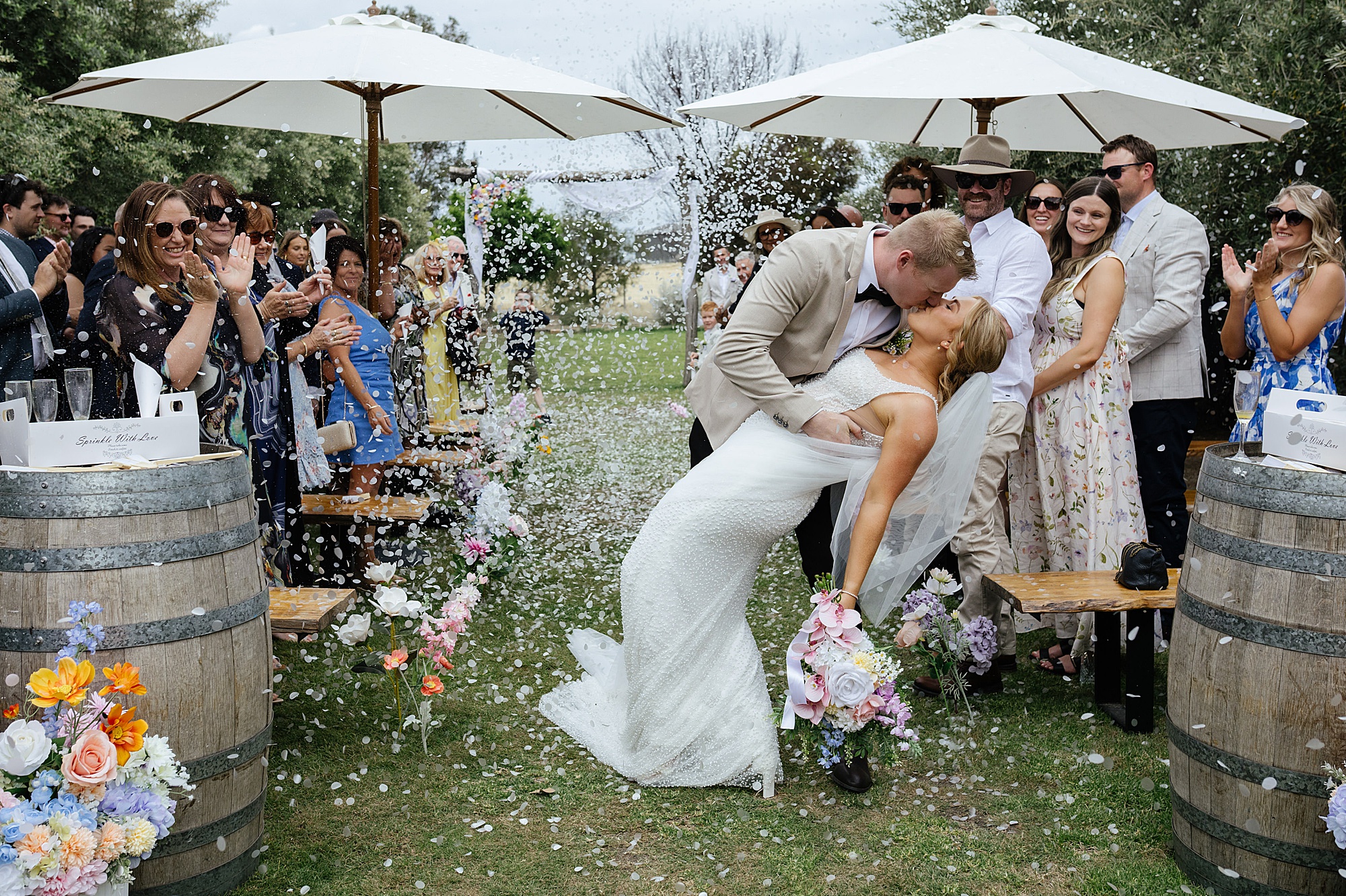 Bride and groom dip kiss while being thrown with confetti at their wedding at Charm Lodge.