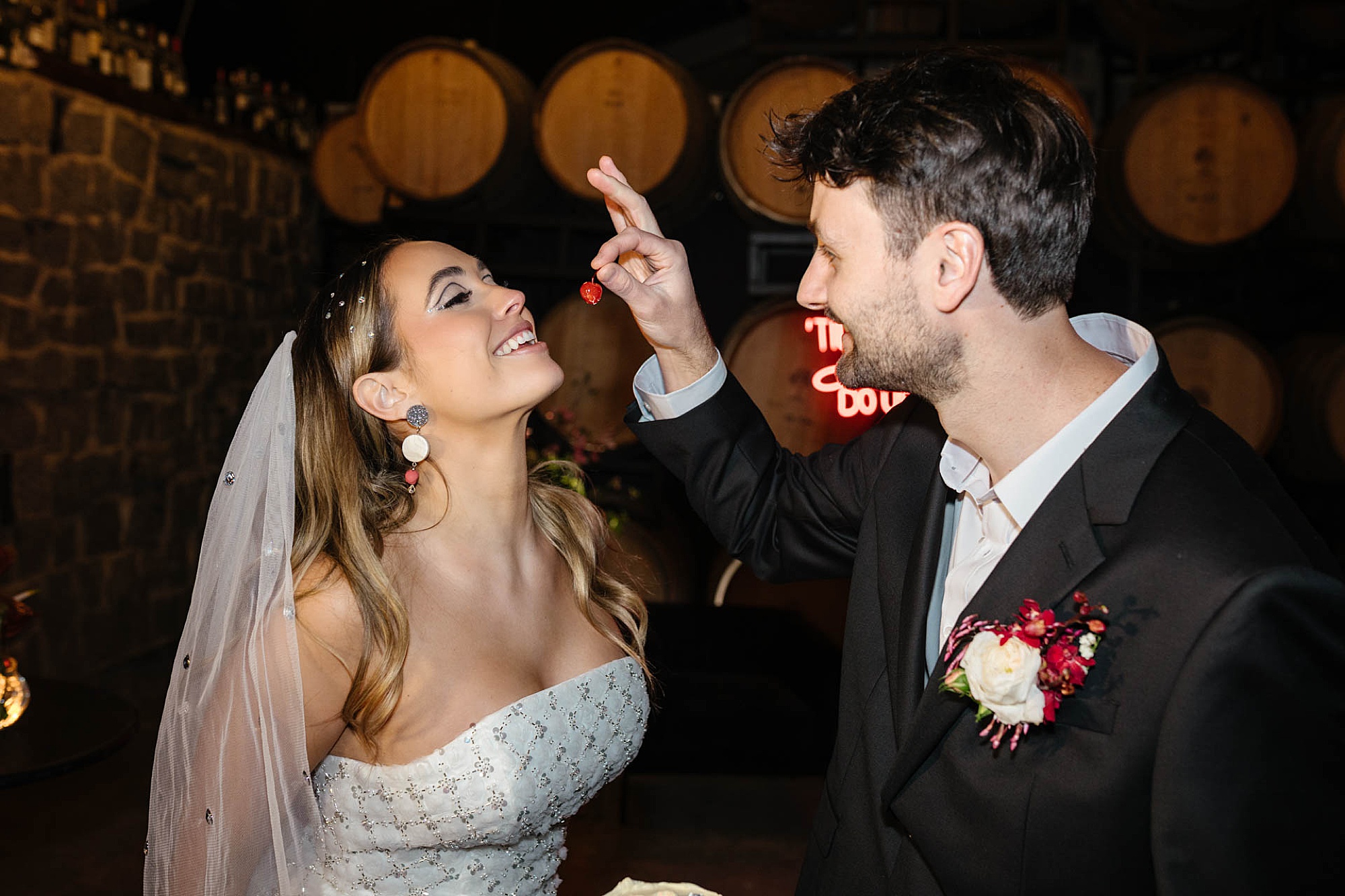 Playful moment at a disco-themed wedding as the groom feeds the bride a cherry, surrounded by retro décor and party vibes.