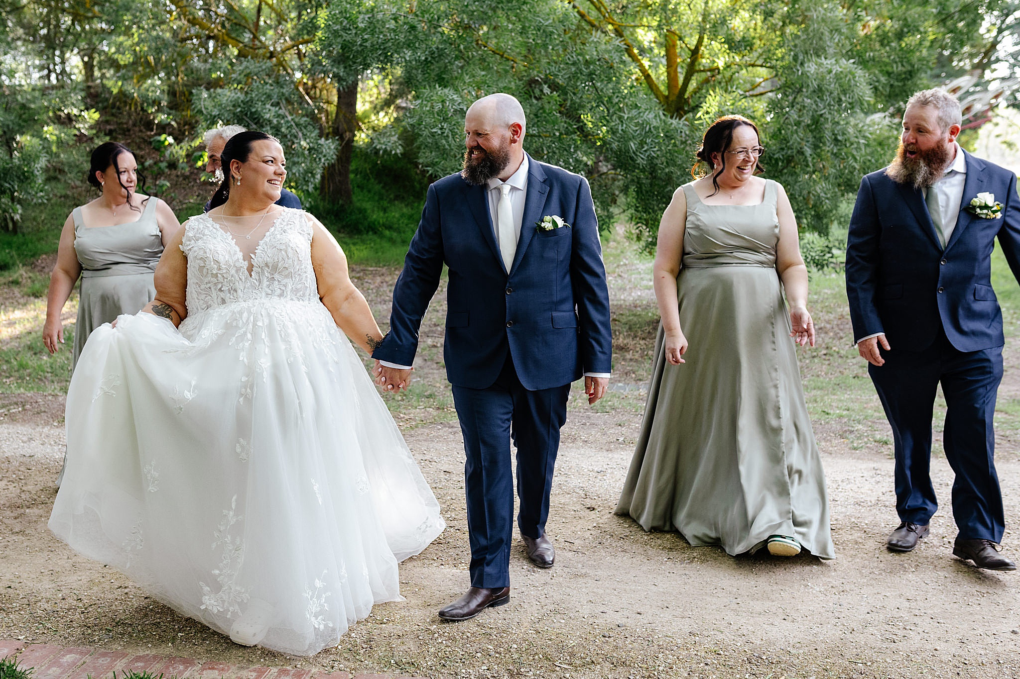 Bride & groom walking on gravel road with bridesmaids next to them.