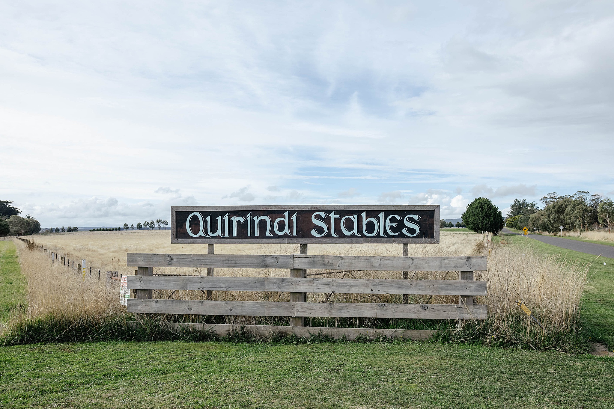 Quirindi Stables sign with picturesque paddocks in the background, showcasing the property’s peaceful rural setting.