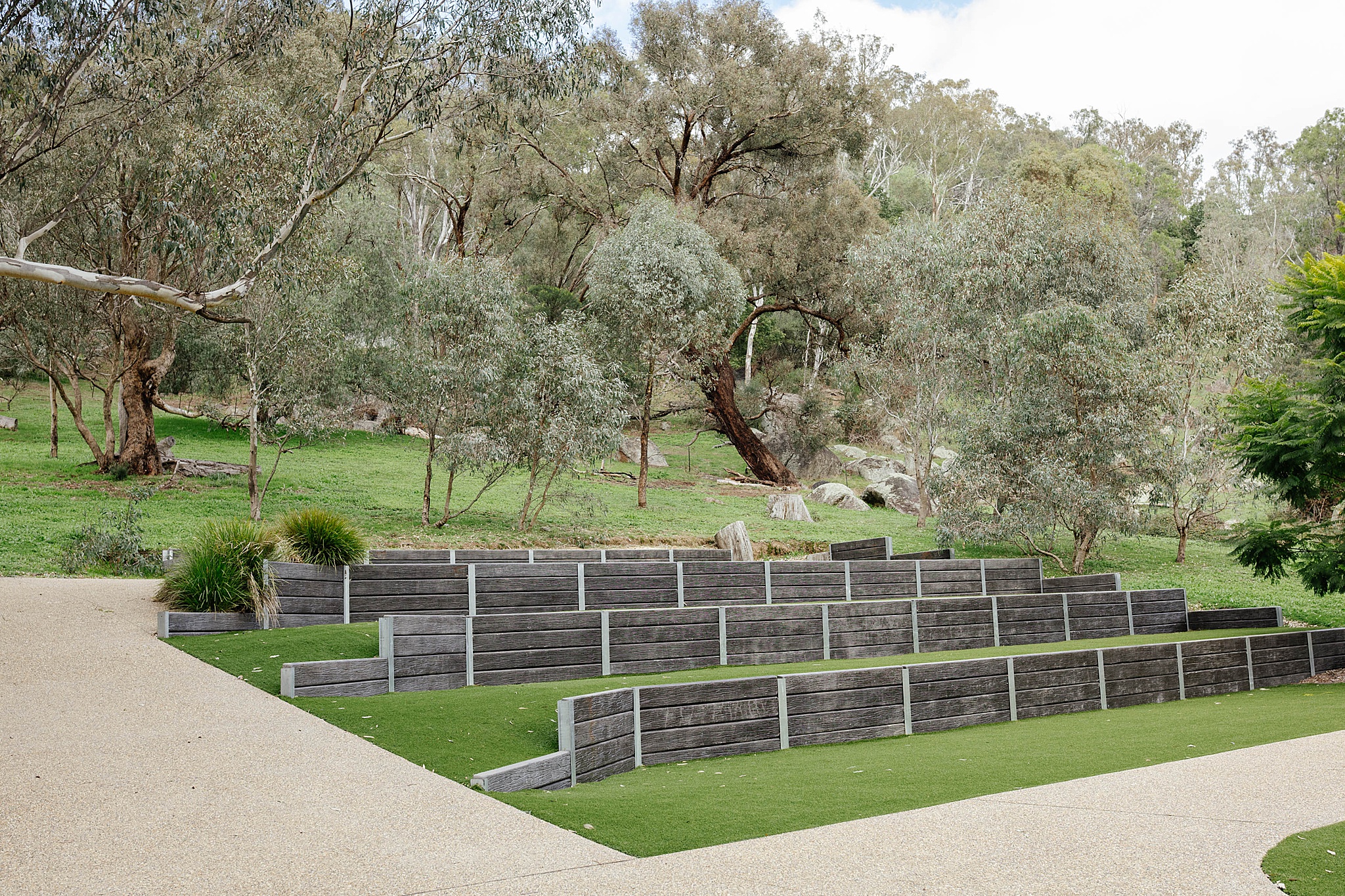 Outdoor wedding ceremony space featuring tiered lawn terraces with retaining walls, allowing guests to sit on different elevations overlooking the ceremony area.